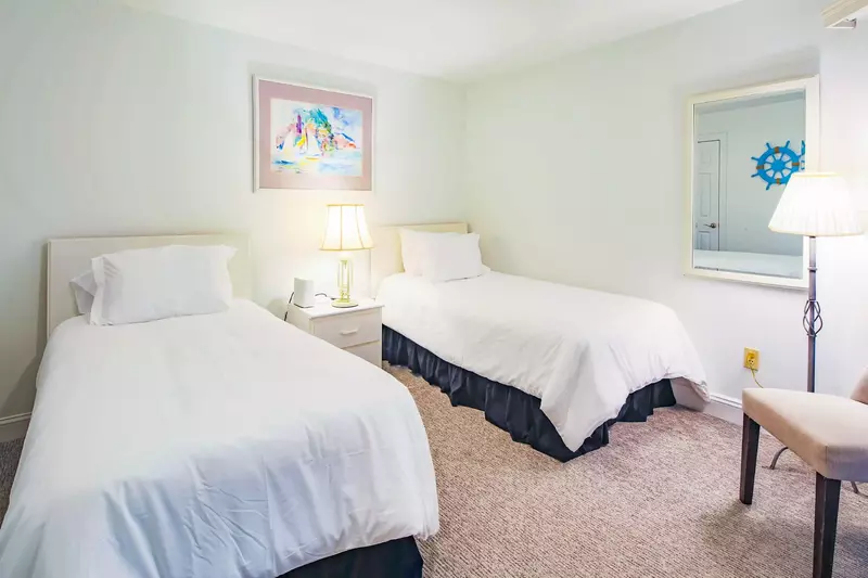 The guest bedroom features two twin beds, a mirror, chair and floor lamp.