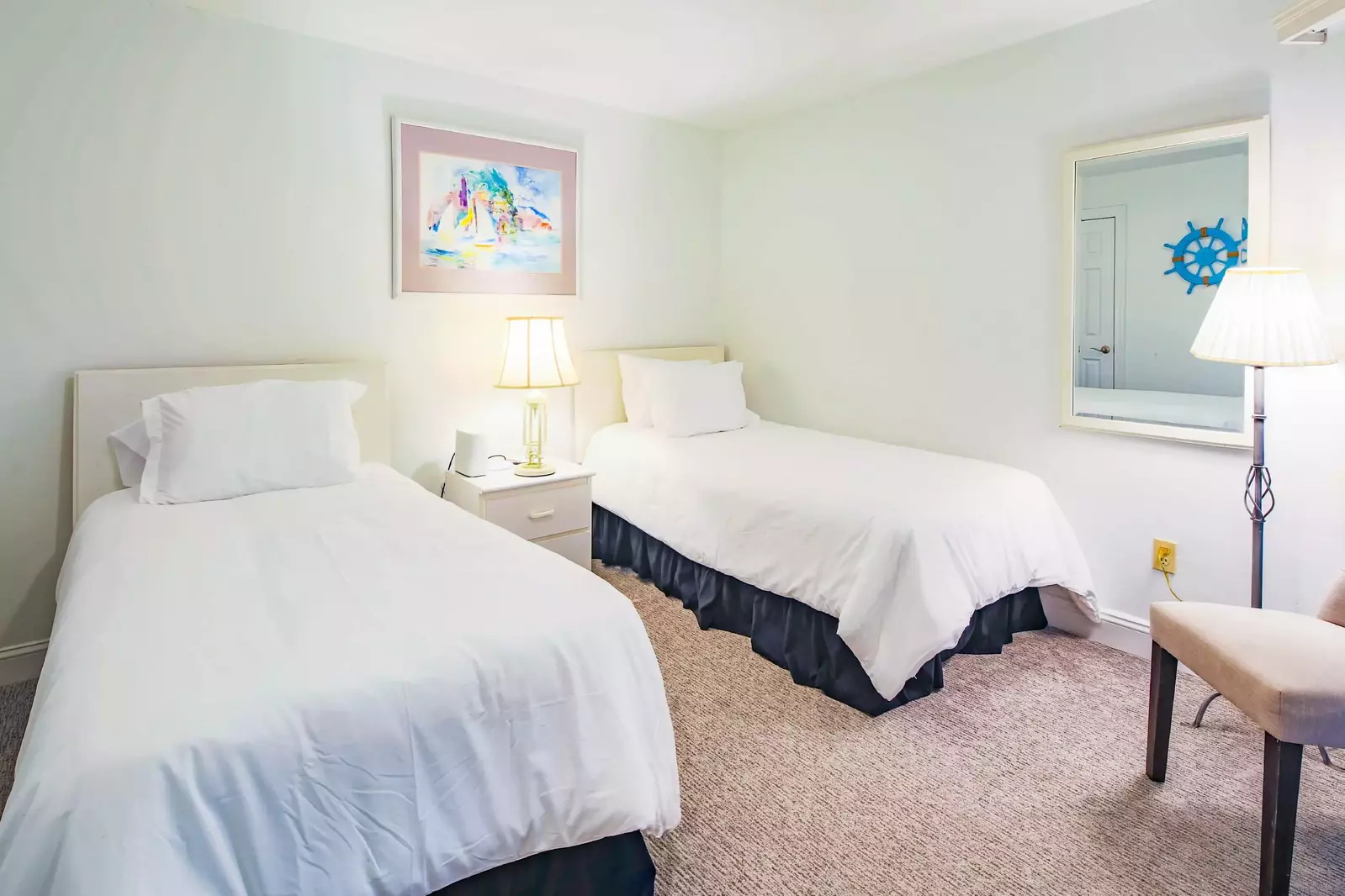 The guest bedroom features two twin beds, a mirror, chair and floor lamp.