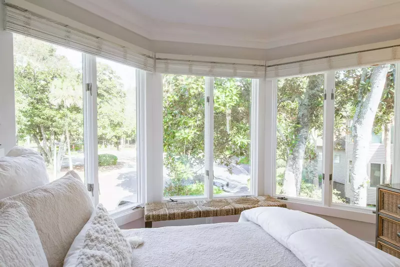 There is a bench and dresser near the wall of windows in the guest bedroom.