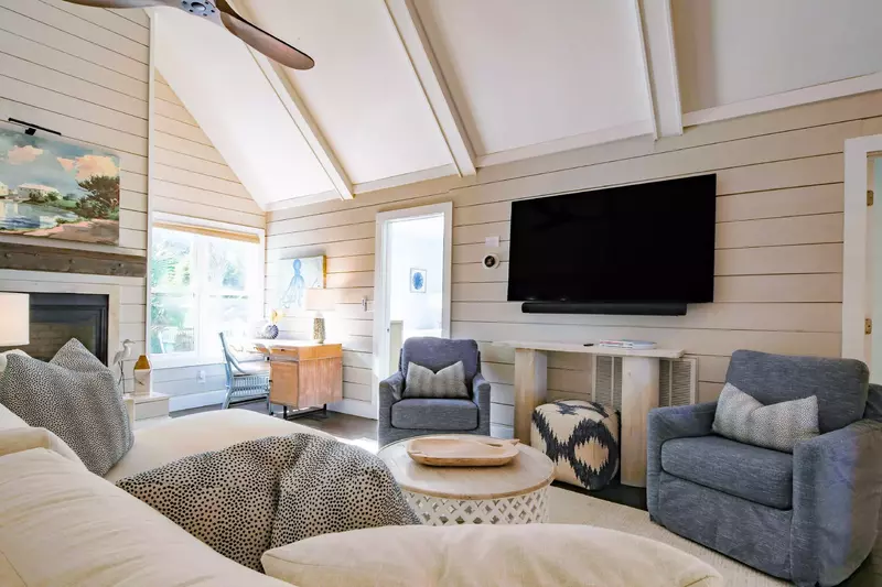 The living room features a wall-mounted smart TV, sectional, two arm chairs and a desk.