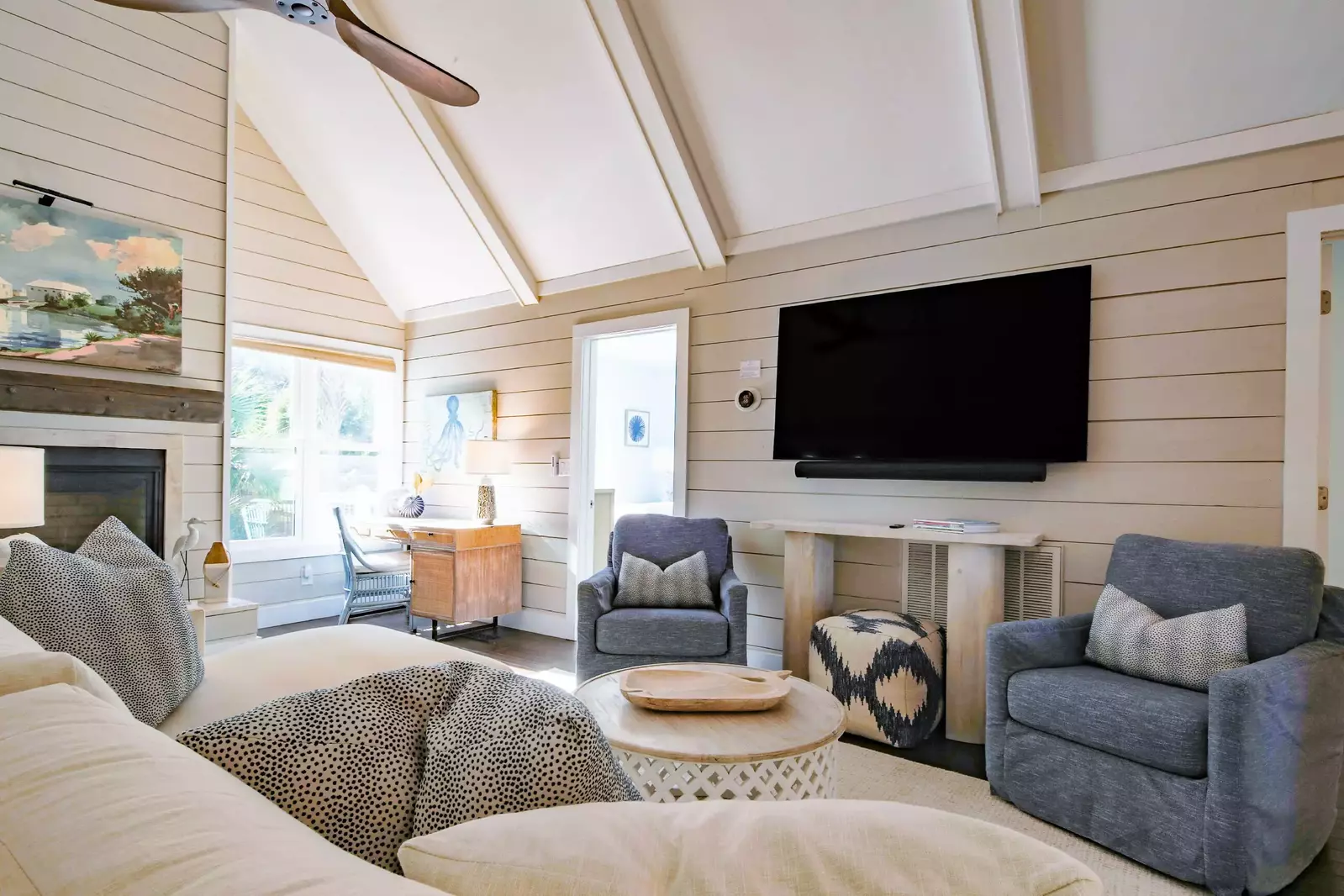 The living room features a wall-mounted smart TV, sectional, two arm chairs and a desk.