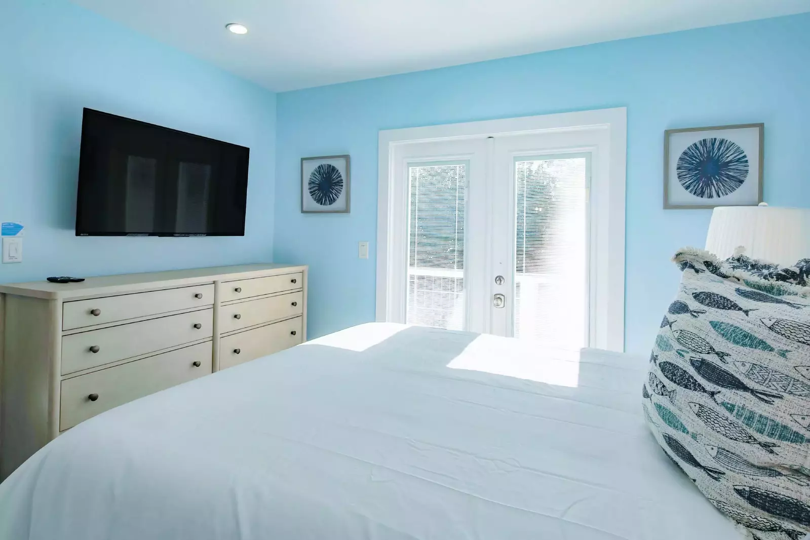 The primary suite also features a dresser, wall-mounted smart TV and access to a private outdoor balcony.