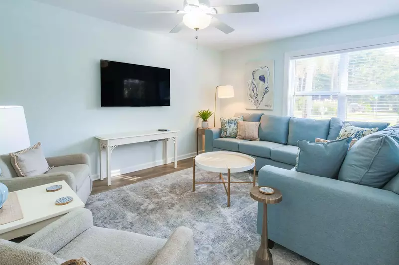 The living room features a spacious sectional, mounted smart TV and arm chairs.