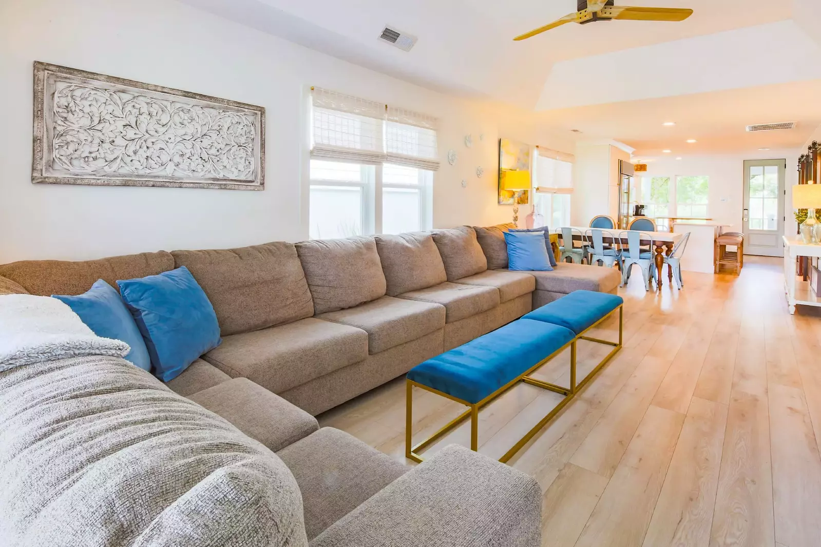 The living room features a tray ceilng, expansive sectional sofa and ceiling fan.