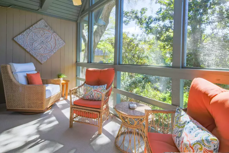 There are three cushioned arm chairs and two end tables on the screened porch.