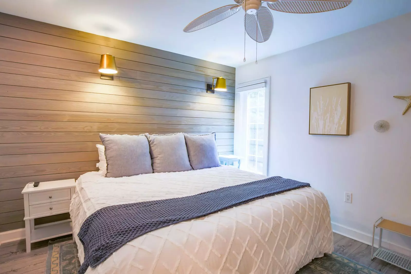 The bedroom features a king bed, night stands, wall scones and ceiling fan.
