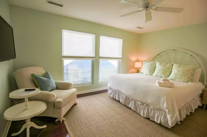 The master suite features a king bed, an arm chair and a ceiling fan.