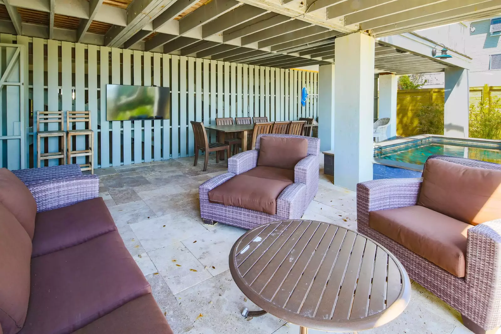 There is an outdoor dining table, wall-mounted TV and cushioned seating area on the patio.