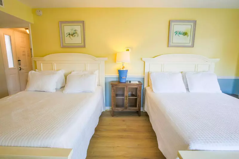 A nightstand with a reading lamp separates the two queen beds.