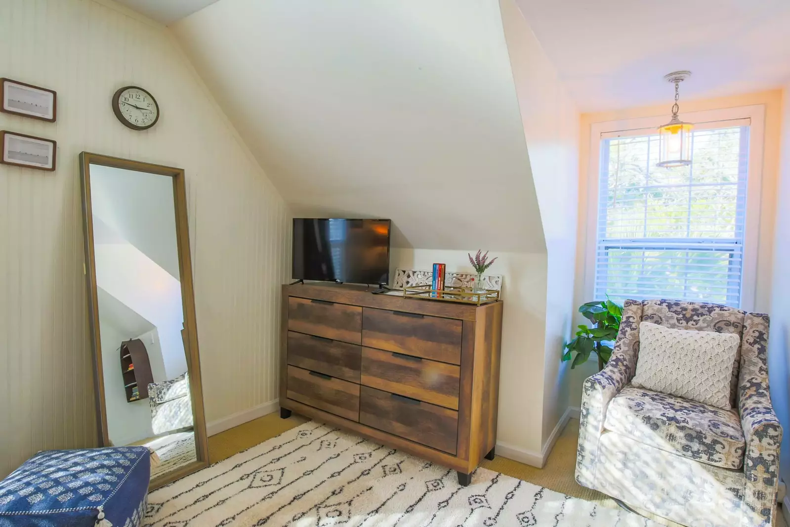 This guest bedroom also features a dresser, a smart TV and an arm chair.