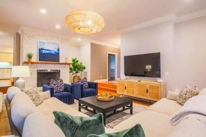 The living room features a spacious sectional, mounted large screen TV and arm chairs.