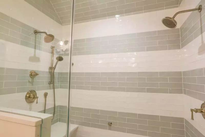 This beautifully tiled walk-in shower in the master suite features two shower heads and a handheld sprayer.