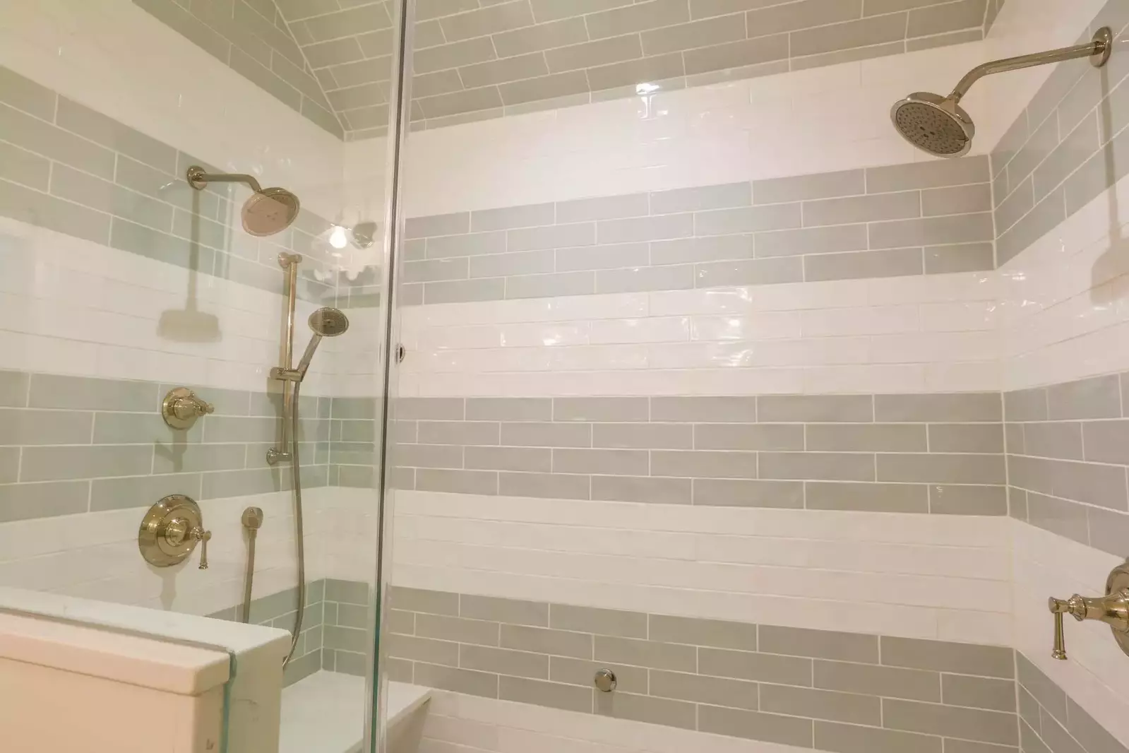 This beautifully tiled walk-in shower in the master suite features two shower heads and a handheld sprayer.