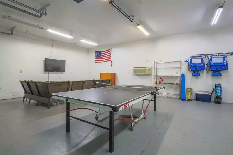 The garage features a mounted smart TV, sectional seating area and a ping pong table.