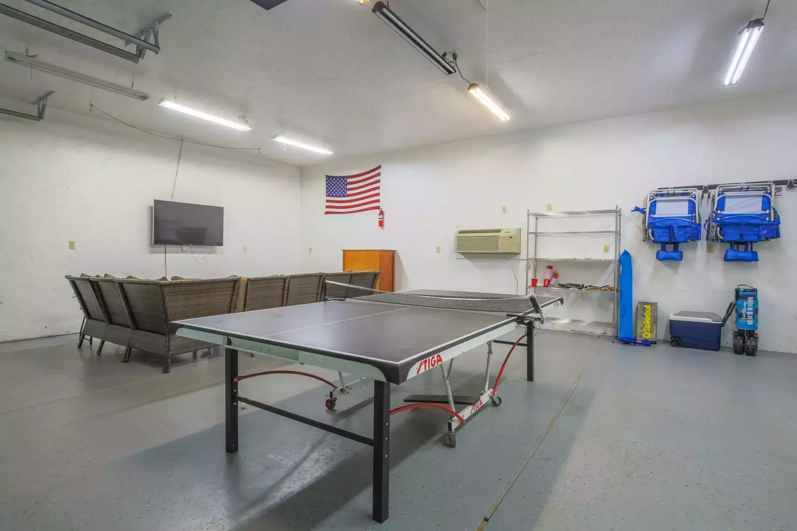 The garage features a mounted smart TV, sectional seating area and a ping pong table.