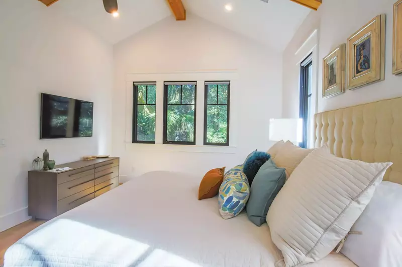 The primary bedroom also features a wall-mounted smart TV, ceiling fan and hardwood floors.