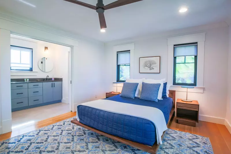 This guest bedroom features a queen bed, hardwood floors and an en suite bathroom.