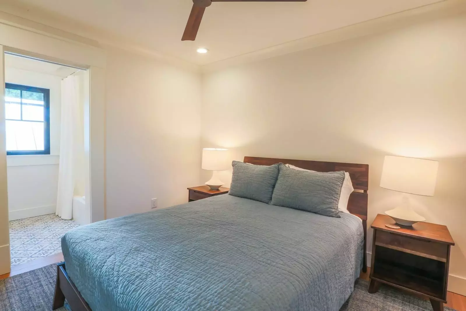 This guest bedroom features a queen bed, night stands with reading lamps, en suite bathroom and a ceiling fan.