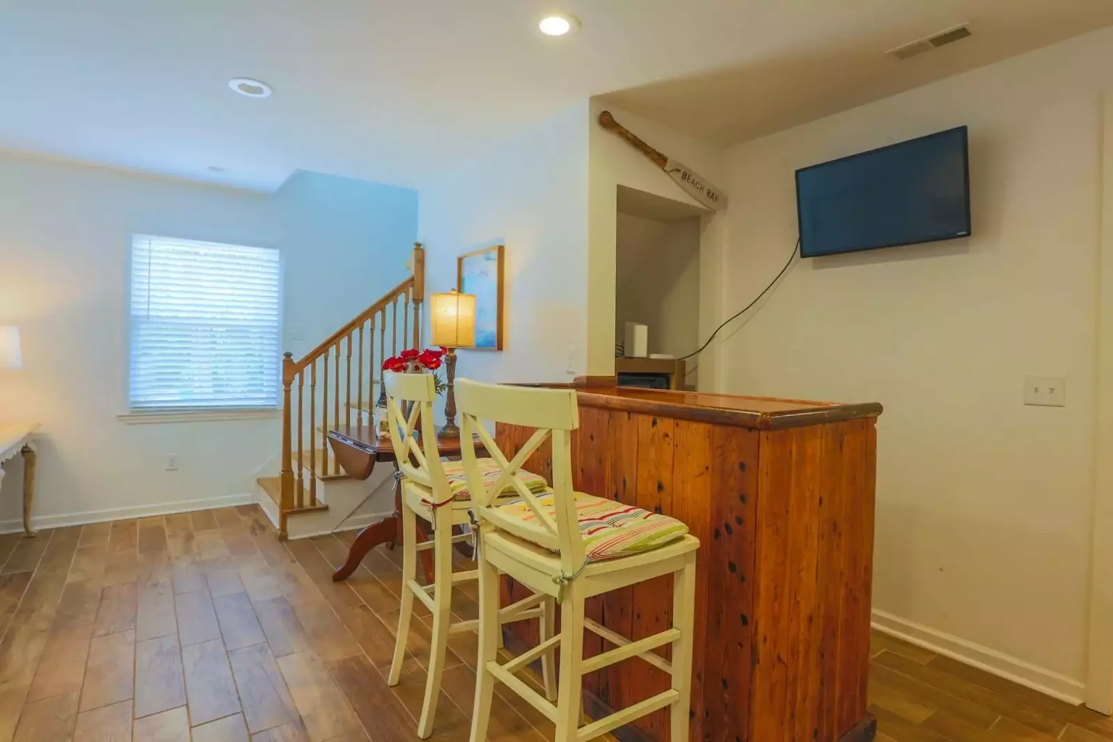 There is a mounted smart TV, high top stools and small bar area near the staircase to the second floor.