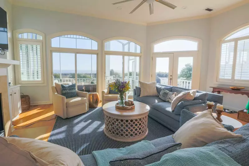 The living room has comfortable seating and arched windows looking out onto the beach.