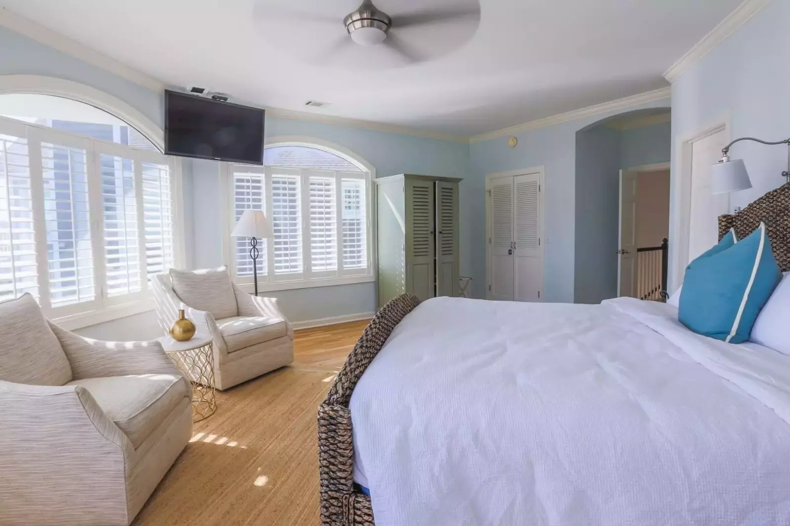 The master bedroom has a seating area, mounted TV and ceiling fan.