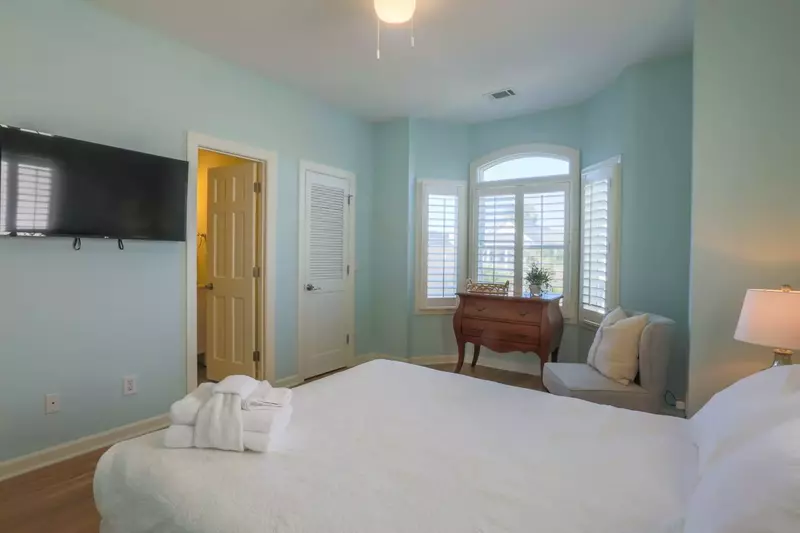 This guest bedroom also features a mounted TV, dresser and an en suite bathroom.