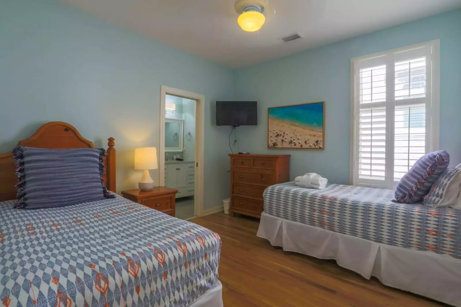 The fourth bedroom in A Golden Sunrise features two twin beds, a dresser and a mounted TV.