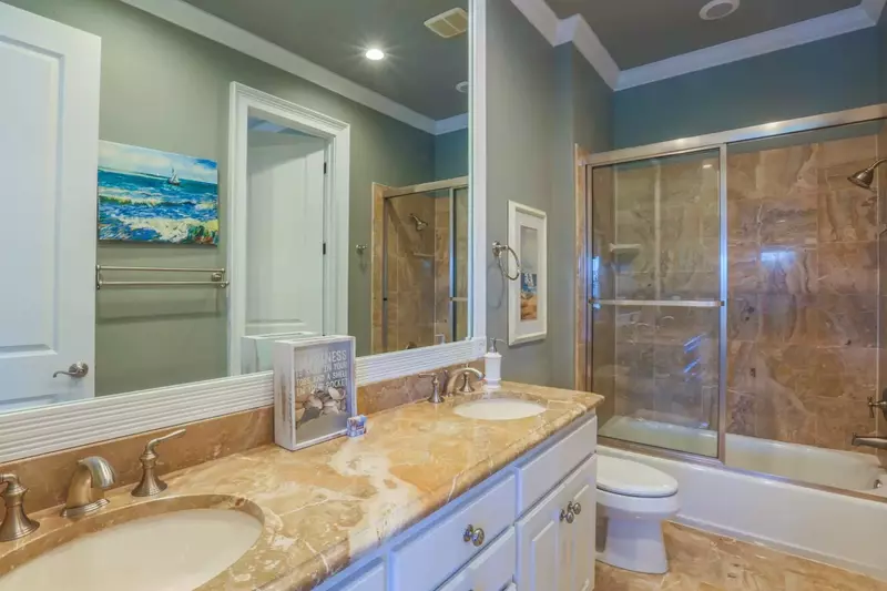 This en suite bathroom features a double sink, marble-topped vanity and a beautifully tiled shower/tub combo.