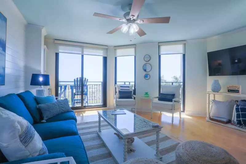 The living room features a mounted, large screen TV and comfortable coastal furnishings.