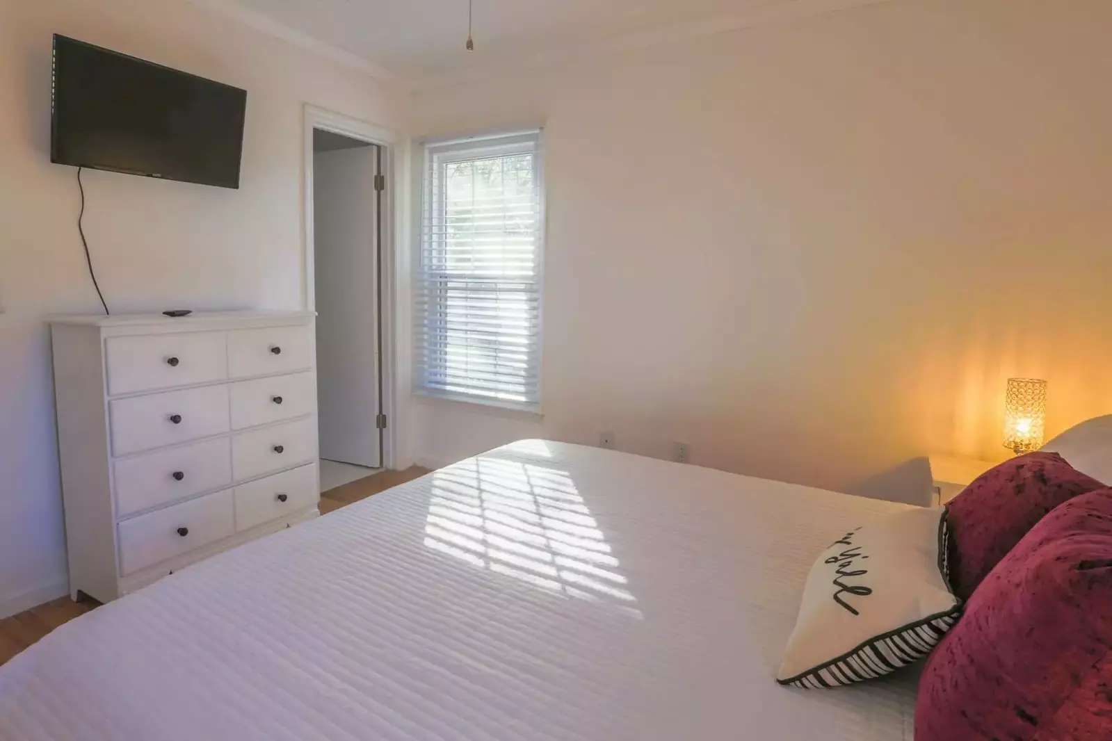 The master bedroom has a mounted smart TV, dresser and an en suite bathroom.
