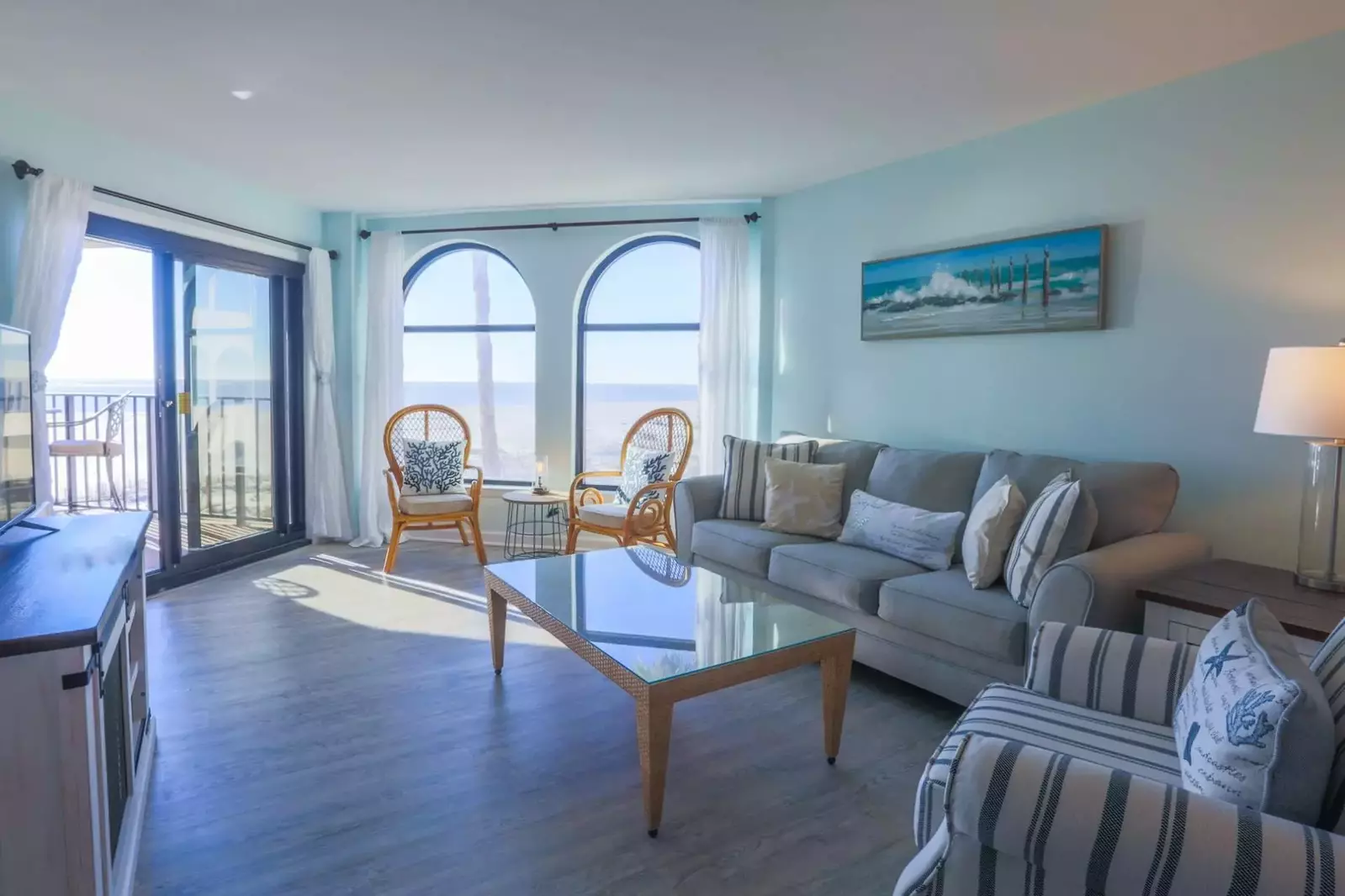 The living room has comfortable seating and two arch windows looking out onto the beach.