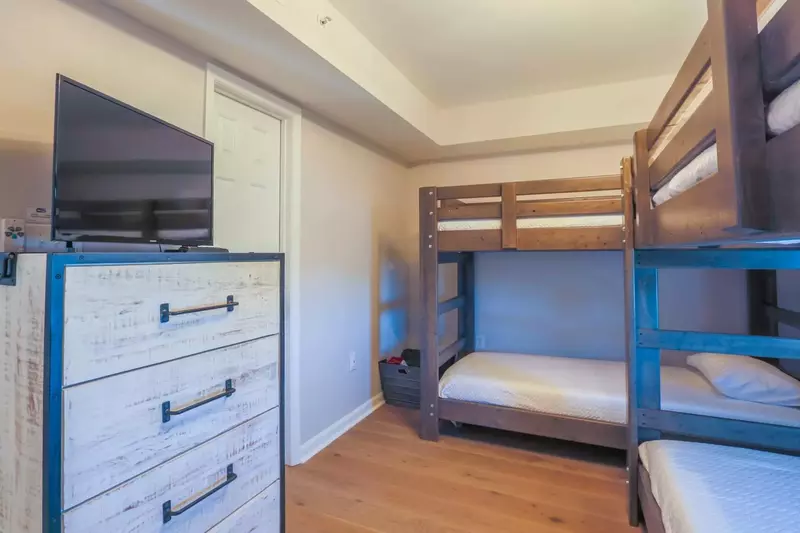 The bunk bedroom features four twin XL beds and a dresser with a smart TV.