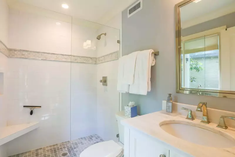This en suite bath has a vanity with white marble countertops, tile flooring and a walk-in tiled shower.
