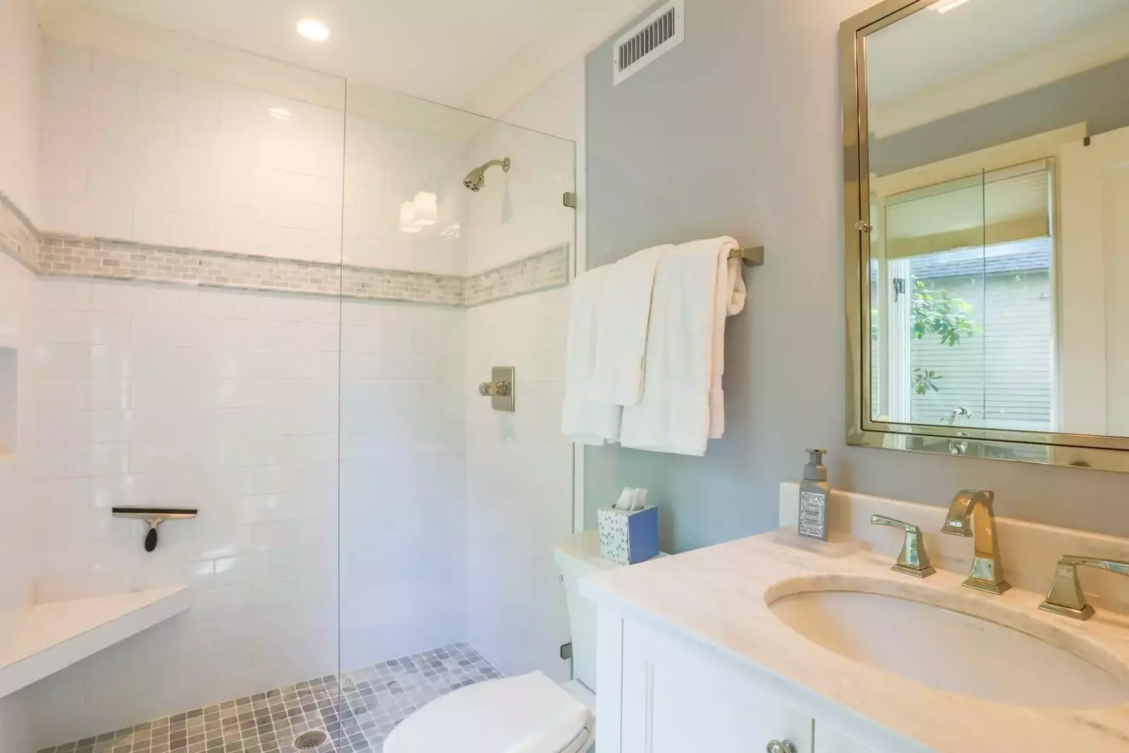 This en suite bath has a vanity with white marble countertops, tile flooring and a walk-in tiled shower.
