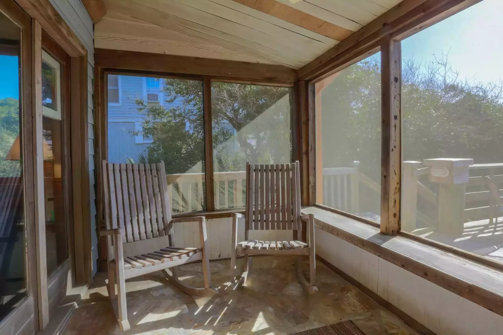 The screened-in porch that separates the house from the deck features two wooden rocking chairs and a bench.