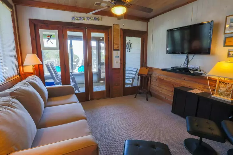 The living room features a large screen TV with Roku, wood paneling, beachy decor and comfortable seating.