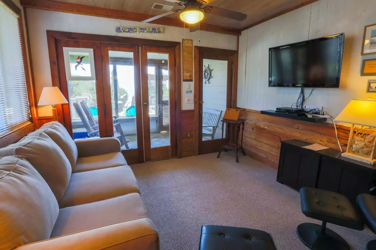 The living room features a large screen TV with Roku, wood paneling, beachy decor and comfortable seating.
