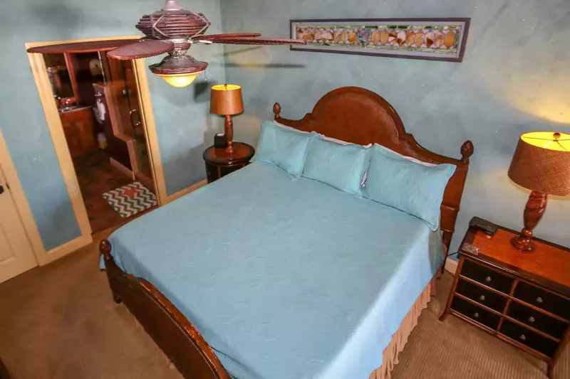 The master bedroom has a king sized bed, carpeted floors and ceiling fan.