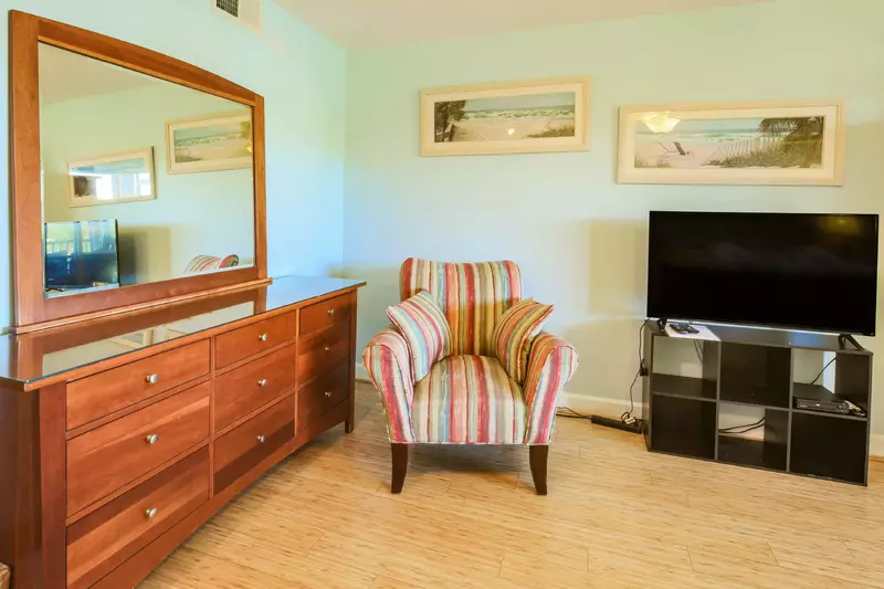 There is an arm chair in the master suite near the dresser and smart TV.