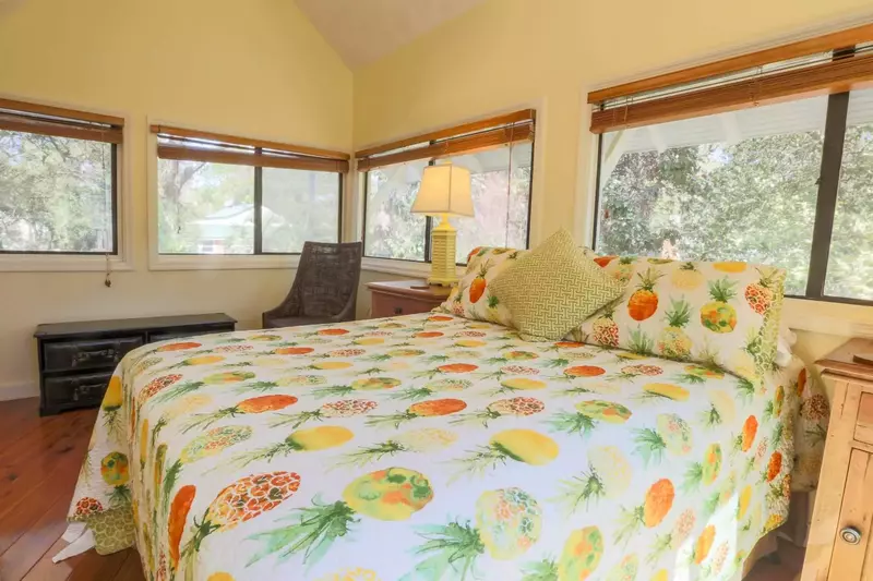 This bright & cheery guest bedroom has three walls of windows & sliding glass doors.