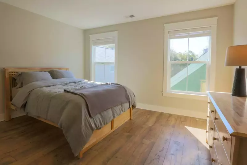 This sunny guest bedroom has a queen-sized bed, dresser and hardwood floors.