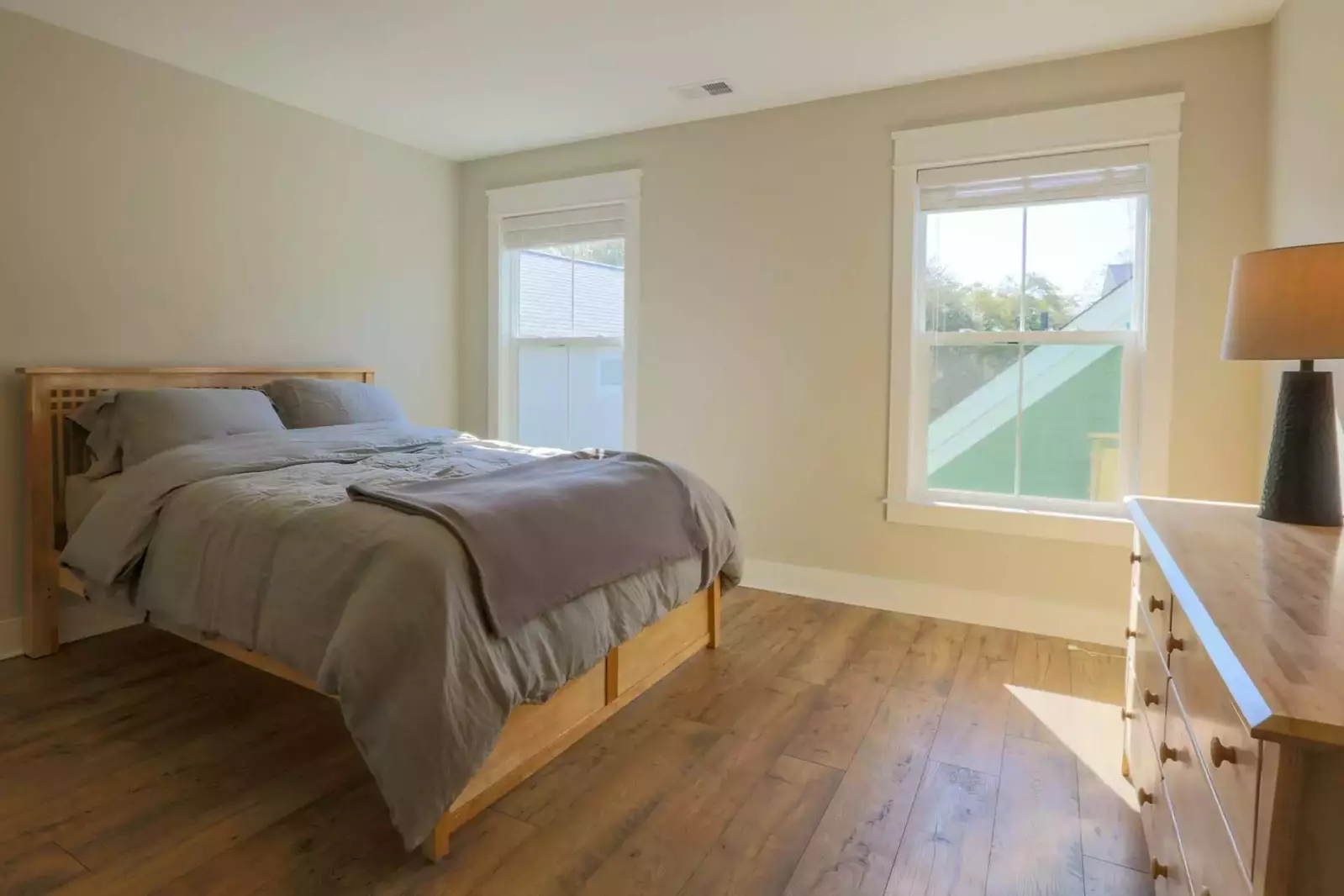 This sunny guest bedroom has a queen-sized bed, dresser and hardwood floors.