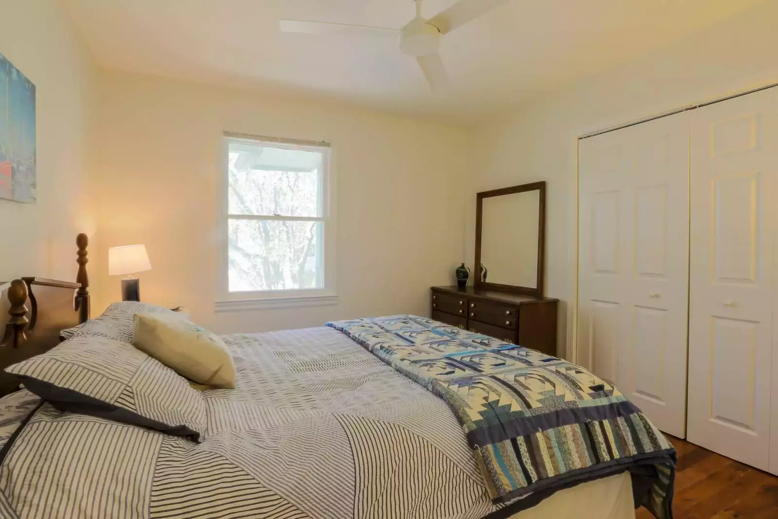 This guest bedroom features a queen bed, dresser, ceiling fan and nighstand with reading lamp.