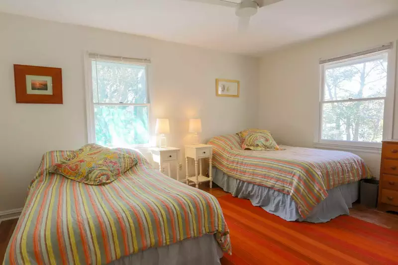 This guest bedroom features two full beds, nightstands with reading lamps, ceiling fan and dresser.