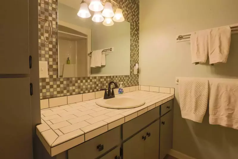 This full bathroom features a combined shower/tub, tiled vanity and ample storage area.