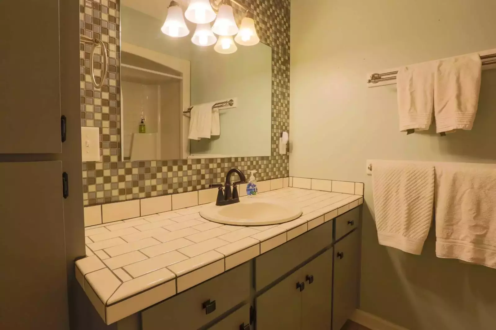 This full bathroom features a combined shower/tub, tiled vanity and ample storage area.
