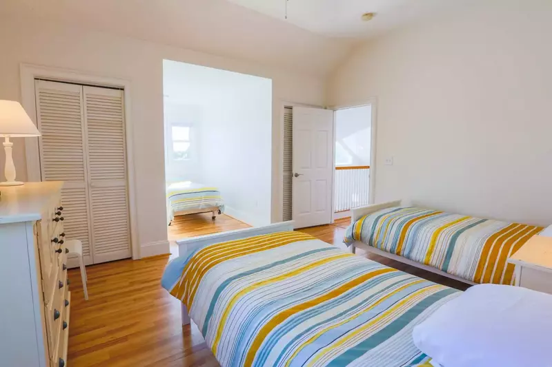 This bedroom has three twin beds, a night stand with reading lamp, dresser and hardwood floors.