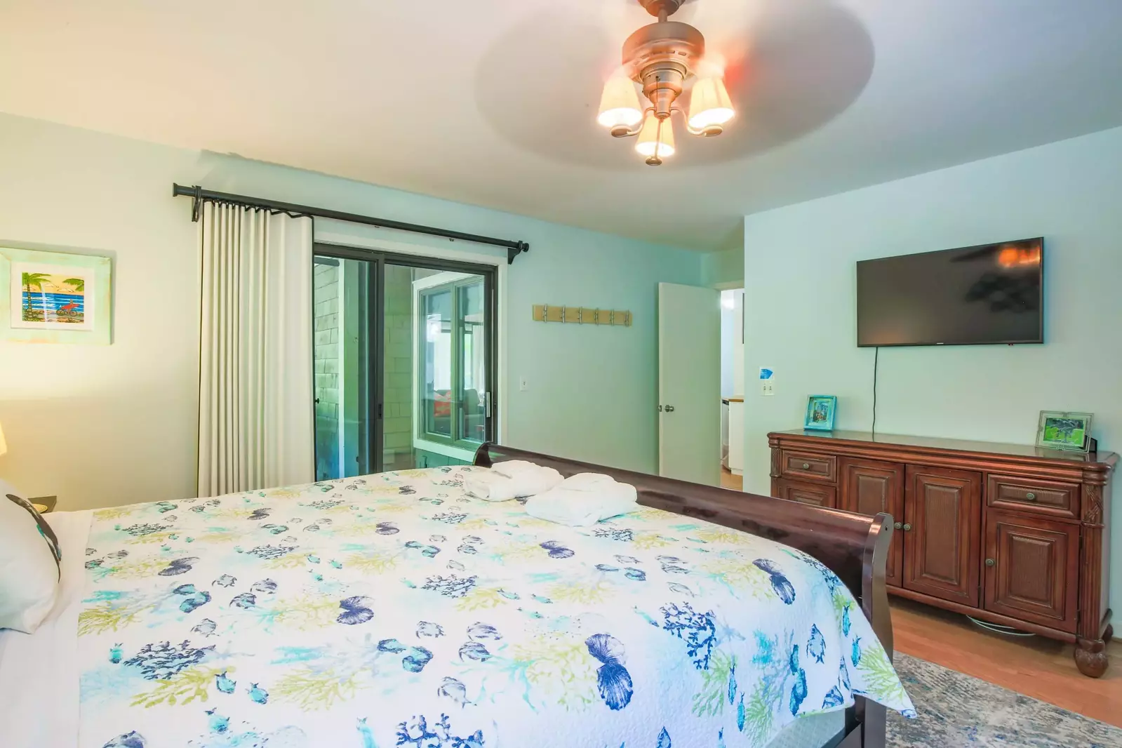 The master suite has a wall-mounted smart TV and sliding door access to the screened porch.