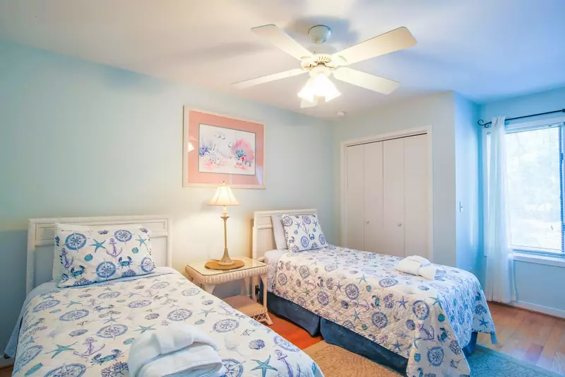 The guest bedroom has two twin beds, a ceiling fan and a night stand with a reading lamp.