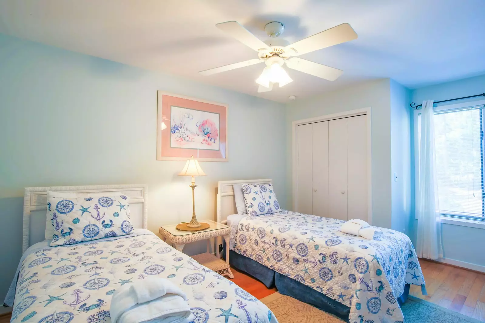 The guest bedroom has two twin beds, a ceiling fan and a night stand with a reading lamp.